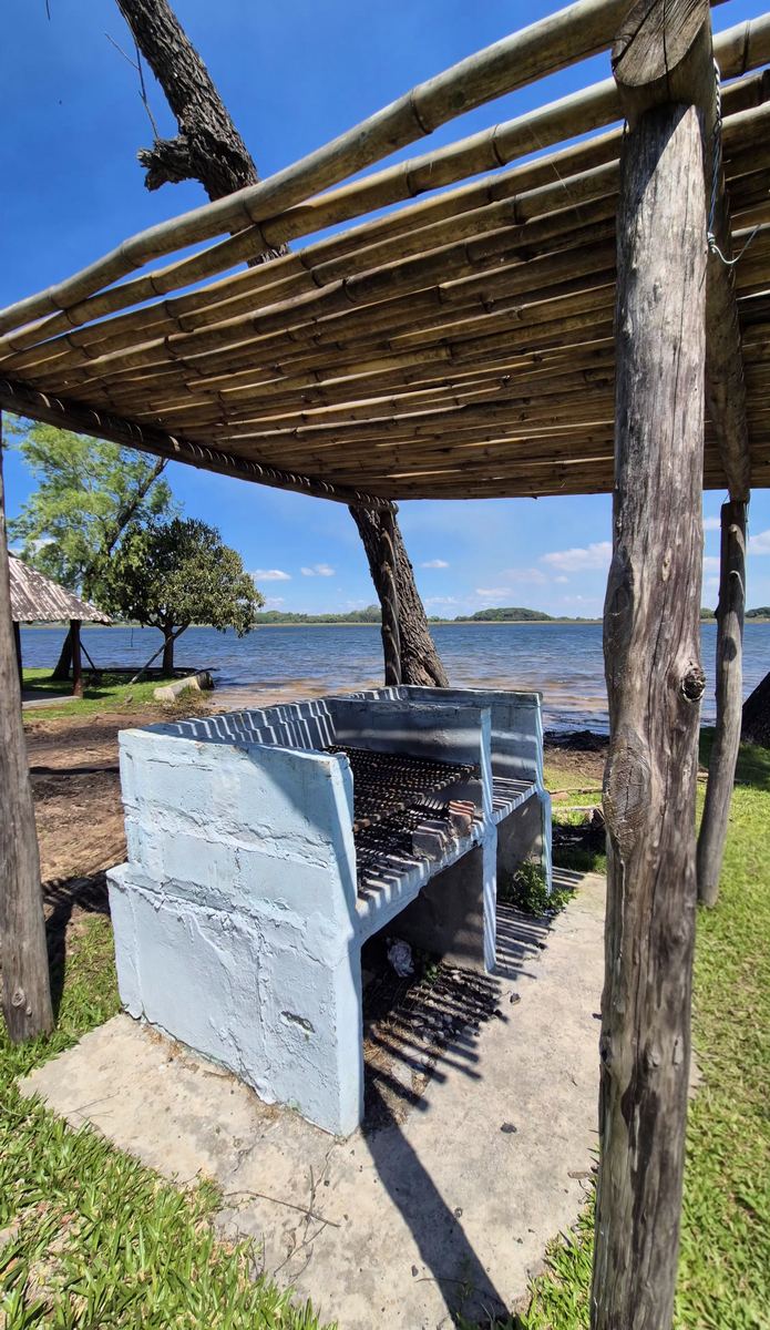 Parrilla de material bajo un techo de troncos, a orillas de la laguna